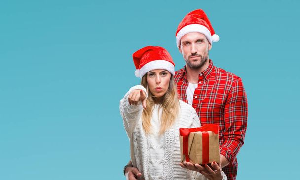 Młoda para w miłości, Boże Narodzenie kapeluszu i trzymając obecny na na białym tle wskazując palcem do aparatu i do Ciebie, ręcznie zarejestrować, gest pozytywny i pewnie z przodu - Zdjęcie, obraz
