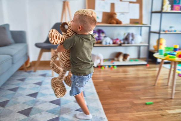 Young caucasian kid playing at kindergarten with stuffed animal. Preschooler boy happy at playroom. - Photo, Image