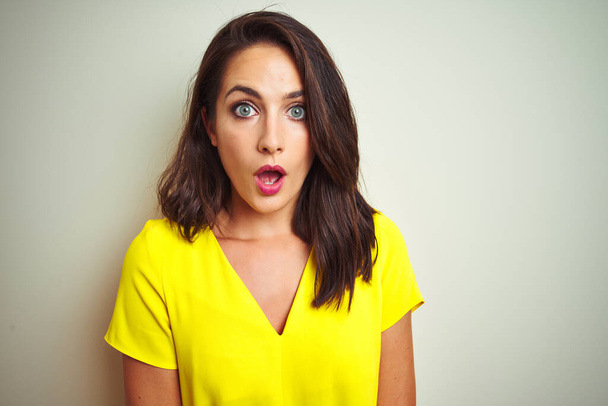 Jonge mooie vrouw dragen gele t-shirt staande over witte geïsoleerde achtergrond bang en geschokt met verrassing expressie, angst en opgewonden gezicht. - Foto, afbeelding
