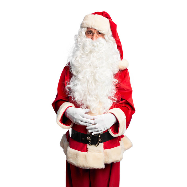 Ein gutaussehender Mann mittleren Alters in Weihnachtsmann-Kostüm und Bart, die Hände zusammengelegt und die Daumen gedrückt, lächelt entspannt und fröhlich. Erfolg und Optimismus - Foto, Bild