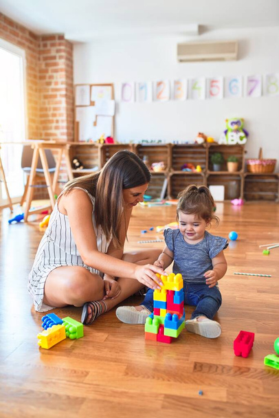 Young beautiful teacher and toddler playing with building blocks toy at kindergarten - Photo, Image