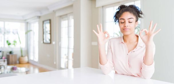 Brede hoek van mooie Afrikaanse Amerikaanse vrouw met afro haar ontspannen en glimlachend met gesloten ogen meditatie gebaar met vingers. Yoga-concept. - Foto, afbeelding