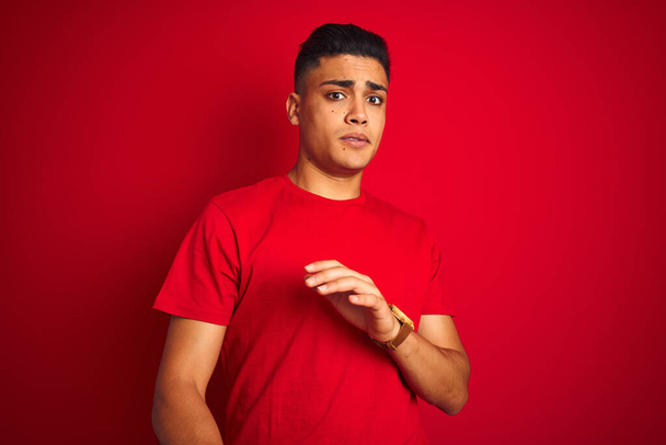 Jeune homme brésilien portant t-shirt debout sur fond rouge isolé expression dégoûtée, mécontent et craintif faire visage dégoût parce que réaction d'aversion. Les mains levées. Concept ennuyeux
. - Photo, image