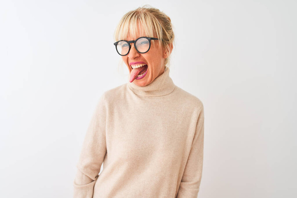 Middle age woman wearing turtleneck sweater and glasses over isolated white background sticking tongue out happy with funny expression. Emotion concept. - Valokuva, kuva