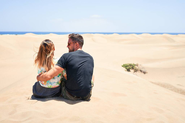 Joven hermosa pareja sentada al revés y abrazándose en la playa
 - Foto, Imagen