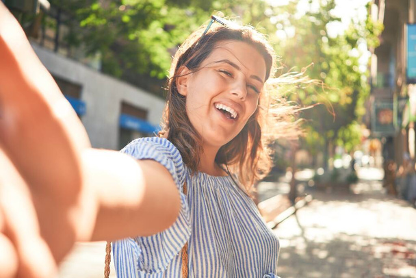 Young beautiful woman smiling happy walking on city streets on a sunny day of summer taking a selfie photo using smartphone - Φωτογραφία, εικόνα
