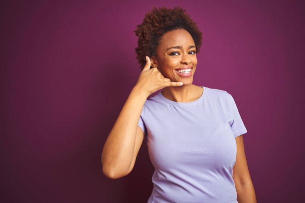 Young beautiful african american woman with afro hair over isolated purple background smiling doing phone gesture with hand and fingers like talking on the telephone. Communicating concepts. - Photo, image