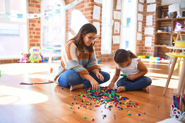 Belle enseignante et tout-petit jouant avec des blocs de construction jouet autour de beaucoup de jouets à la maternelle
 - Photo, image