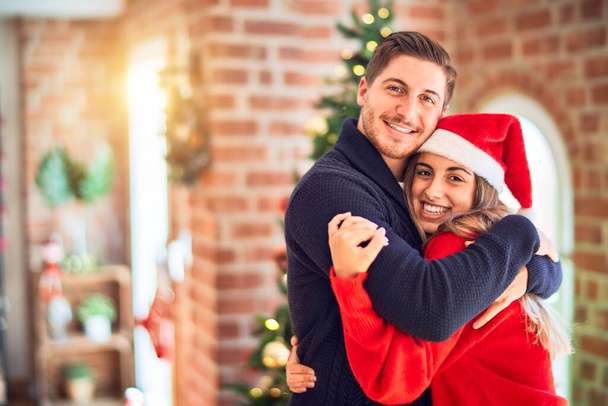 Fiatal szép pár mosolyog boldog és magabiztos. Otthon ácsorog és ölelkezik a karácsonyfa körül. - Fotó, kép