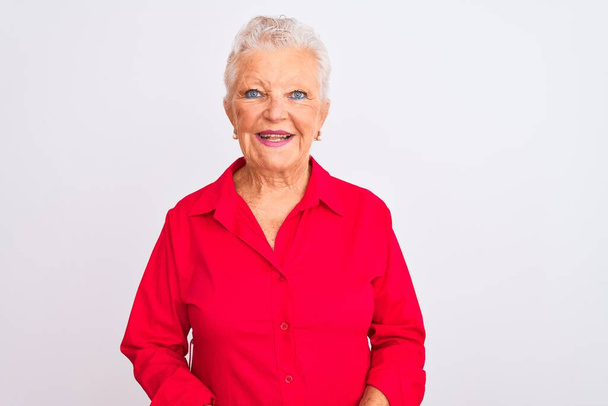 Mujer mayor de cabello gris con camisa informal roja de pie sobre un fondo blanco aislado con una sonrisa alegre y fresca en la cara. Persona afortunada
. - Foto, imagen