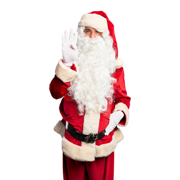gutaussehender Mann mittleren Alters in Weihnachtsmann-Kostüm und Bart stehend und mit Finger Nummer vier nach oben zeigend, während er selbstbewusst und glücklich lächelt. - Foto, Bild