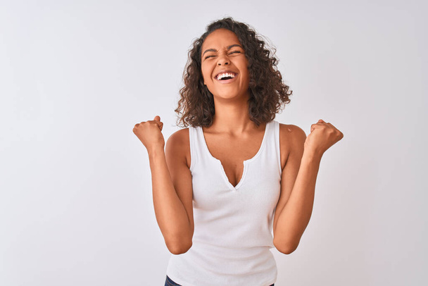 Mujer brasileña joven con camiseta casual de pie sobre un fondo blanco aislado celebrando sorprendida y sorprendida por el éxito con los brazos levantados y los ojos cerrados. Concepto ganador
. - Foto, Imagen