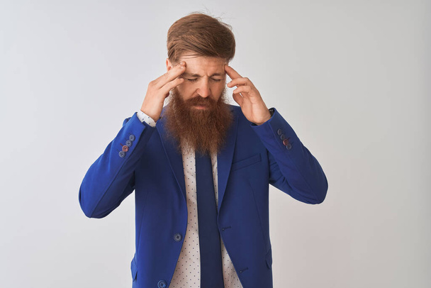 Νεαρός κοκκινομάλλης Ιρλανδός επιχειρηματίας φορώντας κοστούμι στέκεται πάνω από απομονωμένο λευκό φόντο με το χέρι στο κεφάλι για πόνο στο κεφάλι, επειδή το άγχος. Υποφέροντας από ημικρανία. - Φωτογραφία, εικόνα