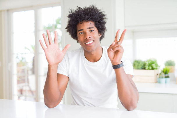 Young african american man wearing casual white t-shirt sitting at home showing and pointing up with fingers number seven while smiling confident and happy. - Photo, Image