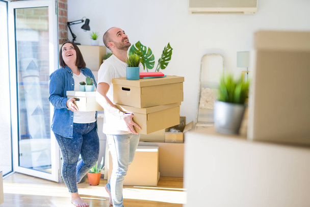 Young couple moving to a new home, smiling happy holding cardboard boxes - Фото, изображение