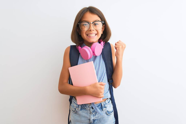 Student child girl wearing backpack glasses book headphones over isolated white background screaming proud and celebrating victory and success very excited, cheering emotion - Foto, Bild