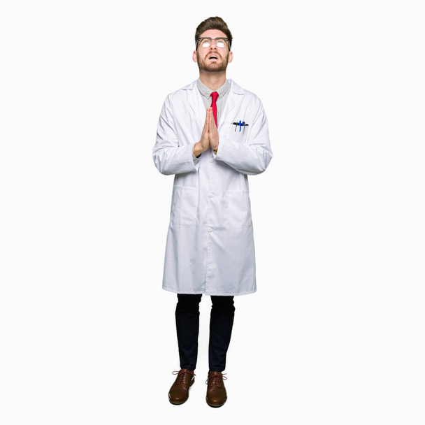 Young handsome scientist man wearing glasses begging and praying with hands together with hope expression on face very emotional and worried. Asking for forgiveness. Religion concept. - Zdjęcie, obraz