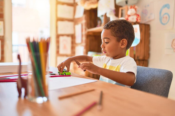 Beautiful african american toddler sitting on desk playing with cars at kindergarten - Photo, Image