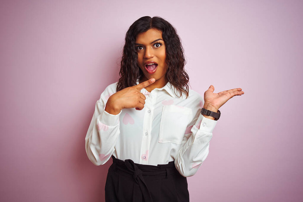 Transsexual transgender businesswoman standing over isolated pink background amazed and smiling to the camera while presenting with hand and pointing with finger. - Foto, afbeelding