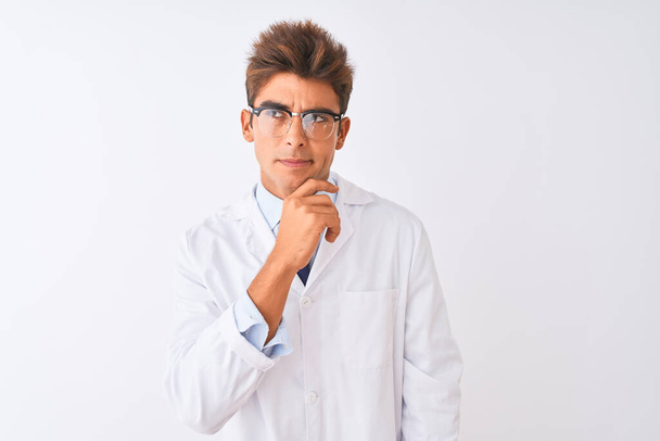 Young handsome sciencist man wearing glasses and coat over isolated white background Thinking worried about a question, concerned and nervous with hand on chin - Photo, Image