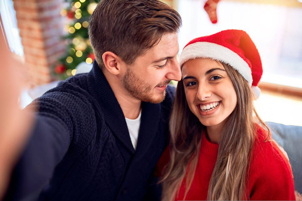 Mladý krásný pár se šťastně a sebevědomě usmívá. Stojící udělat selfie kamerou kolem vánočního stromečku doma - Fotografie, Obrázek