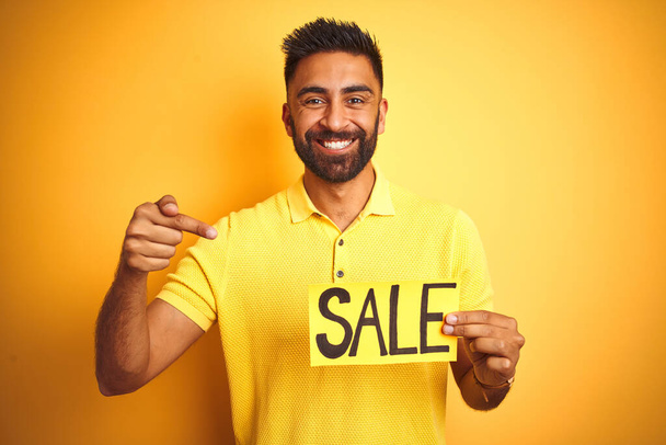 Молодий арабський індійський іспаномовний чоловік тримає рекламний банер над ізольованим жовтим тлом дуже щасливий вказуючи рукою і пальцем
 - Фото, зображення