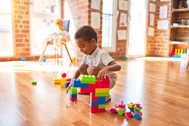 Hermoso niño afroamericano jugando con bloques de construcción sonriendo en el jardín de infantes
 - Foto, Imagen