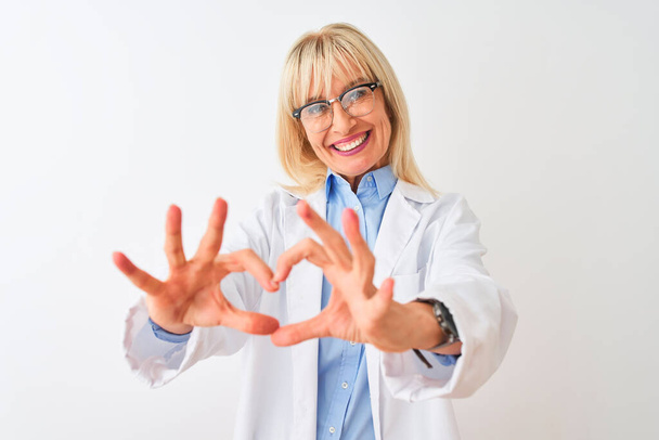 Keski-ikä tiedemies nainen yllään lasit seisoo yli eristetty valkoinen tausta hymyillen rakastunut osoittaa sydämen symboli ja muoto käsin. Romanttinen käsite
. - Valokuva, kuva