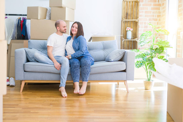junges verliebtes Paar entspannt und umarmt auf dem Sofa im neuen Zuhause sitzend, lächelnd sehr glücklich für den Umzug in eine neue Wohnung - Foto, Bild