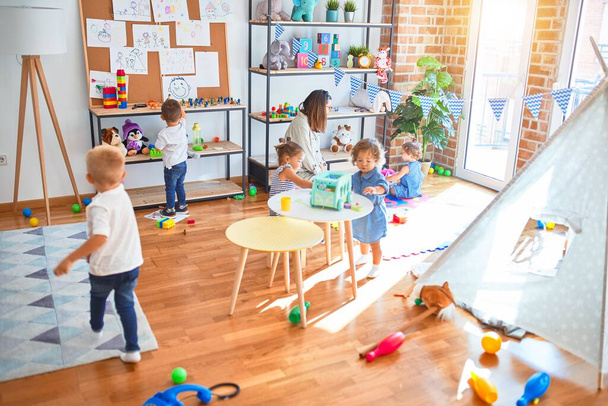 Hermosa maestra y grupo de niños pequeños jugando alrededor de muchos juguetes en el jardín de infantes
 - Foto, imagen