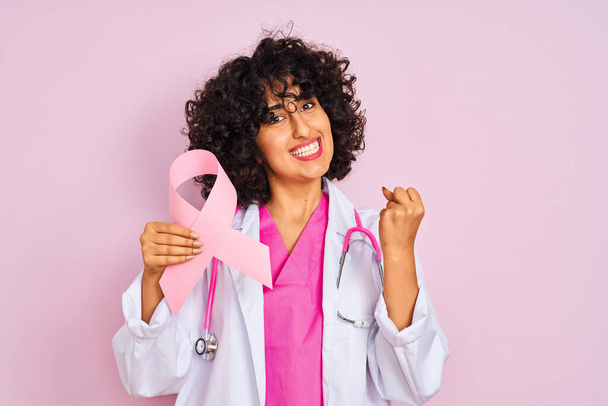 若いですarab医師女性とともに巻き毛保持癌リボン上の隔離されたピンクの背景悲鳴誇りと勝利と成功を祝う非常に興奮,応援感情 - 写真・画像