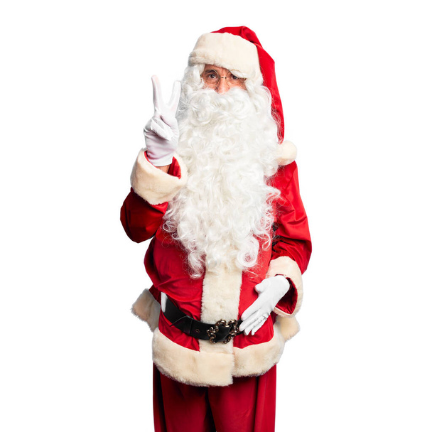 Homem bonito de meia idade vestindo traje de Papai Noel e barba de pé mostrando e apontando para cima com os dedos número dois enquanto sorri confiante e feliz
. - Foto, Imagem
