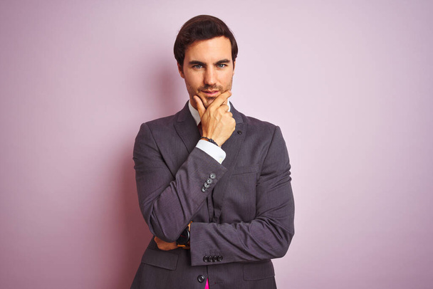 Young handsome businessman wearing suit and tie standing over isolated pink background looking confident at the camera with smile with crossed arms and hand raised on chin. Thinking positive. - Photo, Image