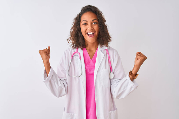 Young brazilian doctor woman wearing stethoscope standing over isolated white background celebrating surprised and amazed for success with arms raised and open eyes. Winner concept. - Foto, imagen