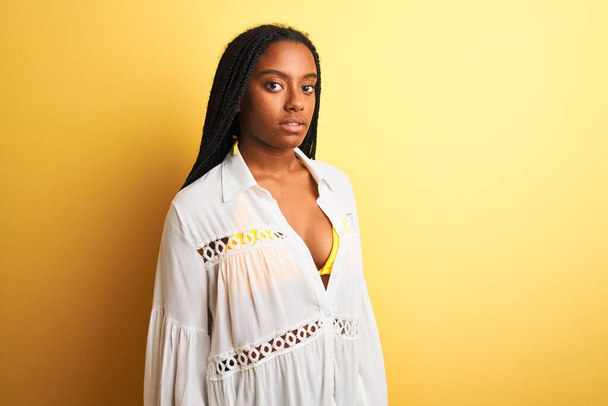 Young african american woman wearing white t-shirt standing over isolated yellow background with a happy and cool smile on face - Photo, Image
