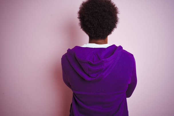 Joven afroamericano vestido con sudadera púrpura de pie sobre un fondo rosa aislado mirando hacia atrás con los brazos cruzados
 - Foto, imagen