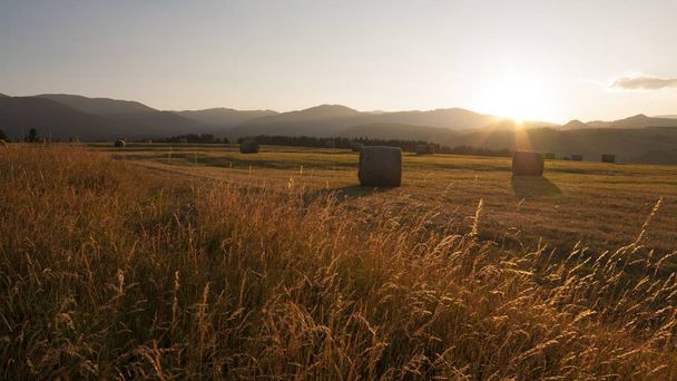 Feno fardos ao nascer do sol, prado e silhueta de belas colinas no fundo
 - Foto, Imagem