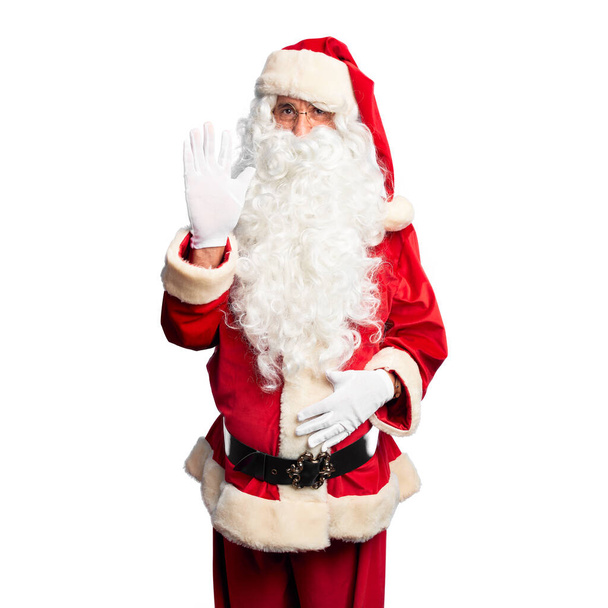 Красивый мужчина средних лет в костюме Санта-Клауса и с бородой, стоя, говорит привет счастливый и улыбающийся, дружелюбный жест приветствия
 - Фото, изображение