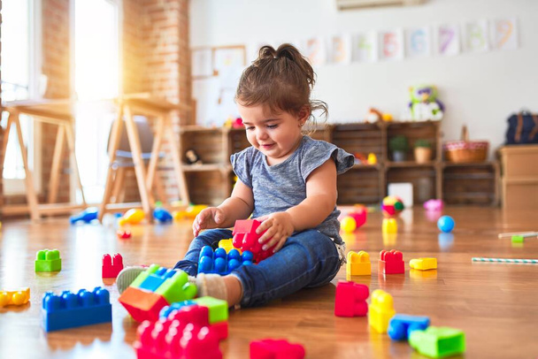 Beau bambin assis sur le sol jouant avec des blocs de construction jouets à la maternelle
 - Photo, image