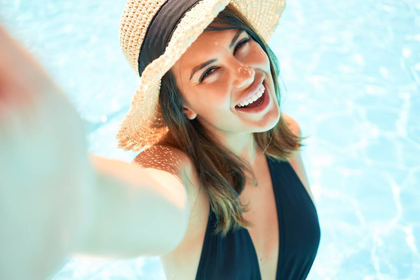 Jovem mulher bonita e sexy na piscina do hotel tomando uma selfie sorrindo usando smartphone no dia ensolarado
 - Foto, Imagem