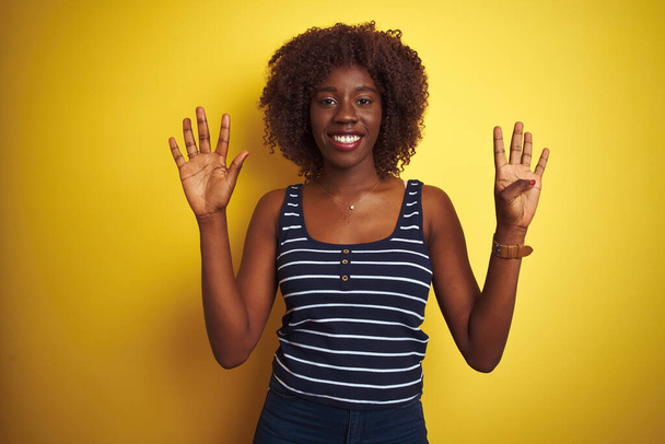 Young african afro woman wearing striped t-shirt over isolated yellow background showing and pointing up with fingers number nine while smiling confident and happy. - Photo, image