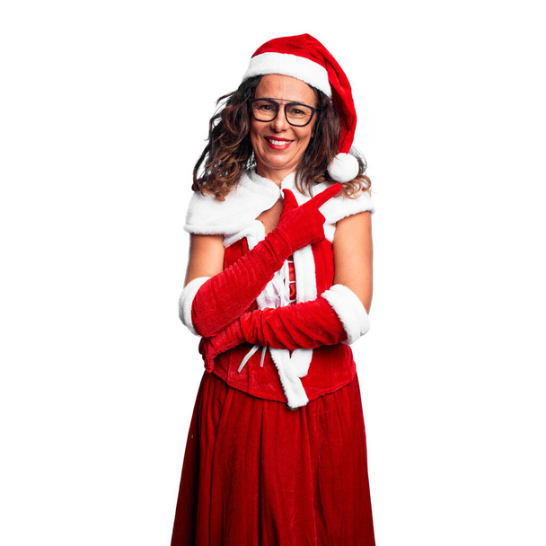 Middle age woman wearing Santa Claus costume cheerful with a smile of face pointing with hand and finger up to the side with happy and natural expression on face - Foto, imagen