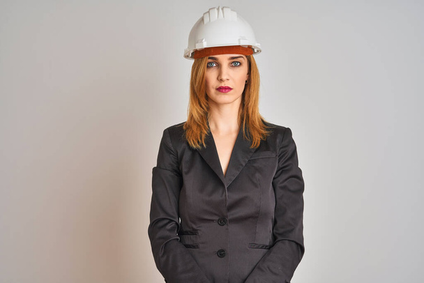 Redhead caucasian business woman wearing safety helmet over isolated background with serious expression on face. Simple and natural looking at the camera. - Valokuva, kuva