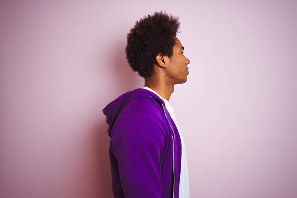 若いですアフリカ系アメリカ人男性身に着けています紫のスウェットシャツ上に立って隔離されたピンクの背景を探しています,リラックスプロファイルポーズとともに自然な顔と自信の笑顔. - 写真・画像