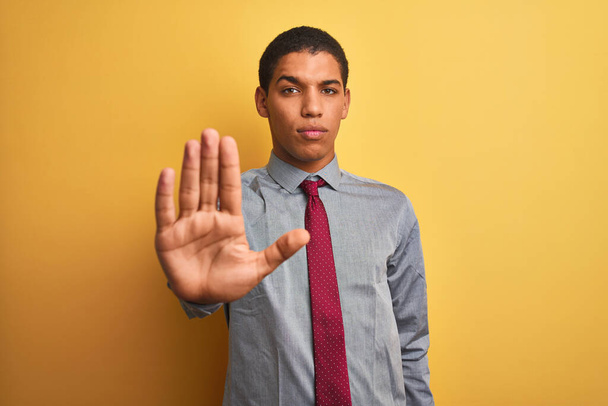 Young handsome arab businessman wearing shirt and tie over isolated yellow background doing stop sing with palm of the hand. Warning expression with negative and serious gesture on the face. - Foto, imagen