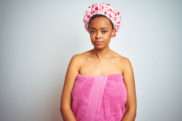 Afrikanische Amerikanerin trägt rosa Duschtuch nach dem Bad über isoliertem Hintergrund entspannt mit ernstem Gesichtsausdruck. einfacher und natürlicher Blick auf die Kamera. - Foto, Bild