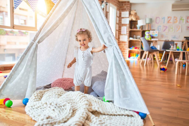 Beautiful caucasian infant playing with toys at colorful playroom. Happy and playful with indian tent at kindergarten. - Photo, Image