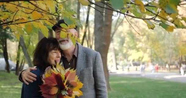 Kucaklaşan mutlu yaşlı çift, sonbaharın tadını çıkarıyor ağaçların arasındaki sıcak bir parkta - yavaş çekimde. - Video, Çekim