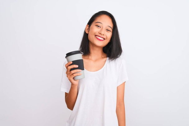 若い中国人女性の飲酒は幸せな顔立ちと歯を示す自信を持って笑顔で笑顔で隔離された白い背景の上にコーヒーのガラスを取ります - 写真・画像