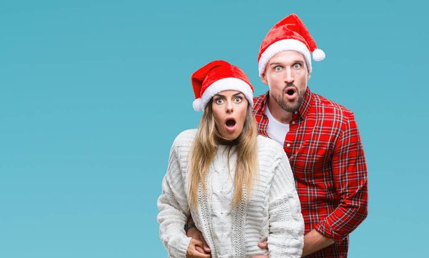 Молодая влюбленная пара в рождественской шляпе на изолированном фоне, напуганная и шокированная удивлением выражением лица, страха и возбужденного лица
. - Фото, изображение